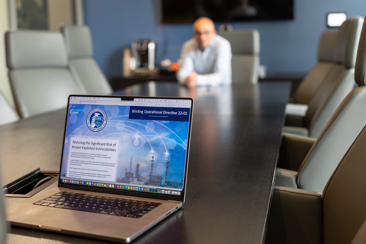 Conference room table with laptop showing CISA webpage & seated man in background Conference room table with laptop showing CISA webpage & seated man in background
